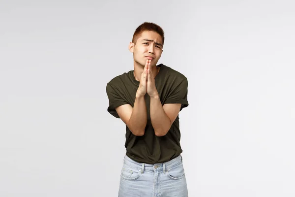 Kleverige taiwanese tiener guy smeken ouders laat hem gaan feest, schudden smeken handen, gesp armen samen in bidden en fronsen, vragen hulp, verontschuldigen, staande grijze achtergrond — Stockfoto