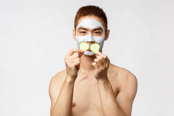 Szépség, bőr és spa koncepció. Portré buta, vicces jóképű ázsiai férfi játszik uborka darab, mint alkalmazni arc maszk és pihentető, megnyugtató pattanások bőr kozmetikai termék — Stock Fotó