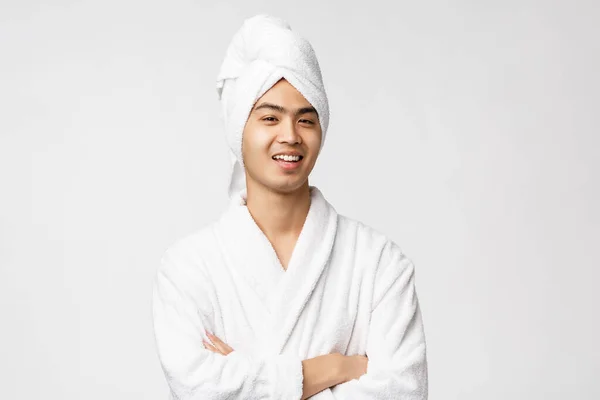 Krása, lázně a volný čas koncept. Portrét pohledného vtipného asijského muže relaxujícího doma, jak si pohodlně obléká župan a ručník přes hlavu, usměvavé potěšení, bílé pozadí — Stock fotografie