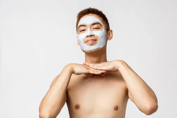 Szépség, bőr és spa koncepció. Portré szép és buta meztelen ázsiai férfi, mosolygós elégedett, visel arc maszk krém, kozmetikai termék vigyáz a bőrre, álló fehér háttér — Stock Fotó