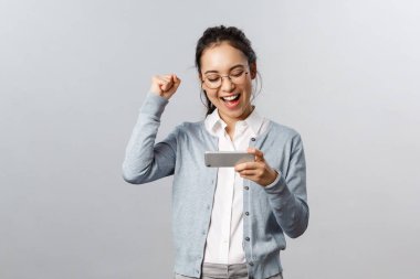 Teknoloji, online ve mobil yaşam tarzı konsepti. Tatmin olmuş, zafer kazanan Asyalı kadın internet oyununda arkadaşlarını yendi, akıllı telefonu tut, yumruk salla ve evet de, başarıyı kutla, bitirme seviyesini