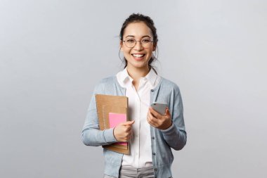 Eğitim, öğretmenler, üniversite ve okul konsepti. Akıllı ve zeki bir bayan öğretmen, elinde akıllı telefon ve kitaplarla, hazırlık dersleri, çalışma materyalleri, gri arka plan.