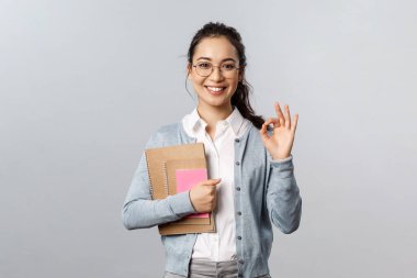 Eğitim, öğretmenler, üniversite ve okul konsepti. Mükemmel okul, online dersimize katıl. Gözlüklü genç kız öğrencinin portresi, tamam işareti göster ve defterleri ödevleriyle birlikte tut