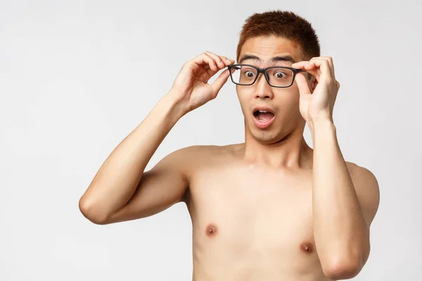 Beauty, people and lifestyle concept. Close-up portrait of shocked young asian man with naked torso, take-on glasses and gasping surprised, seeing something shocking at left, white background — Stock Photo, Image