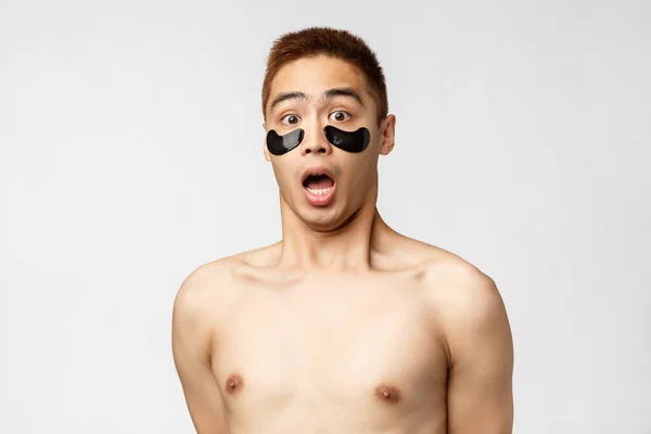 Belleza, gente y estilo de vida. Retrato de sorprendido, joven asiático sobresaltado con torso desnudo y parches en los ojos negros, jadeando asombrado, boca abierta y mirada fija cámara impresionada, fondo blanco — Foto de Stock