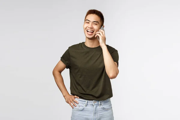 Technologia, styl życia online i koncepcja komunikacji. Portret wesołego śmiejącego się azjaty rozmawiającego z przyjacielem przez telefon komórkowy, śmiejącego się i uśmiechającego jako odwracającego wzrok, szarego tła — Zdjęcie stockowe