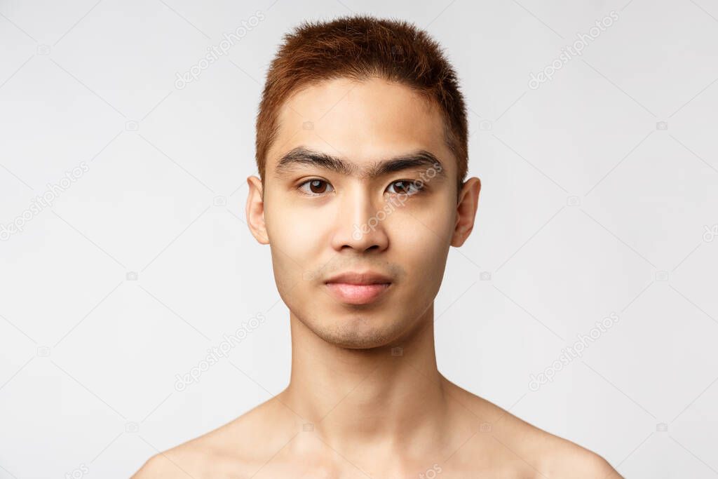 Beauty, skincare and men health concept. Headshot of handsome young asian man with no blemishes, perfect skin condition without acne, smiling enthusiastic, standing white background