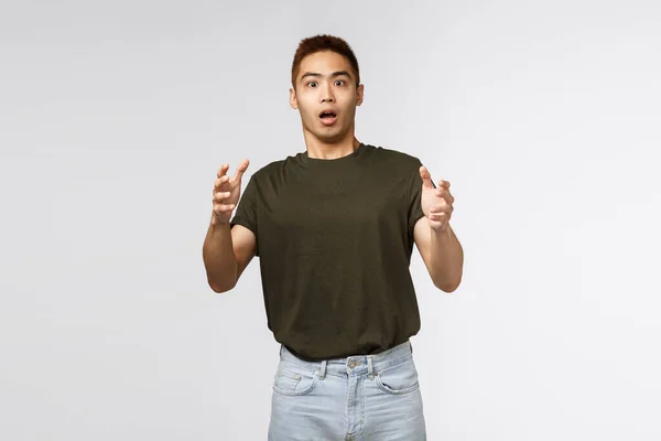 Retrato de chocado jovem do sexo masculino, taiwanese cara pegar produto que a pessoa jogando nele, levantando as mãos para cima e olhar intenso e estressado, ofegante assustado, de pé fundo cinza — Fotografia de Stock