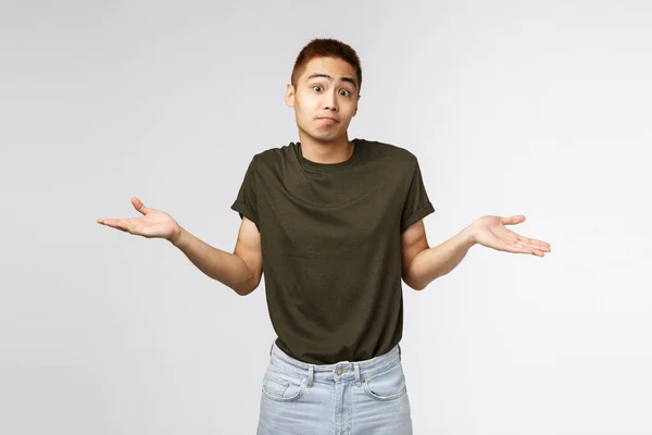 Chi lo sa, non lo so. Ritratto di uomo asiatico scrollato di dosso confuso in t-shirt greey, sorridente e scusante, spiacente non poter aiutare, in piedi perplesso e inconsapevole della situazione, sfondo grigio — Foto Stock