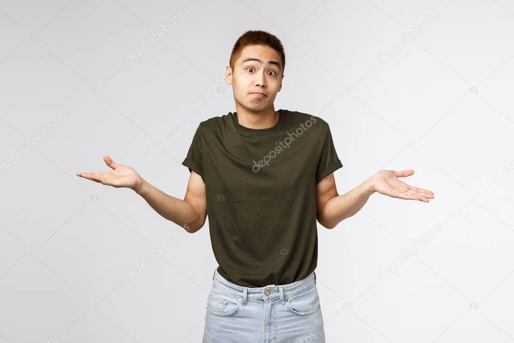 Who knows, I dont aware. Portrait of confused shrugging asian man in greey t-shirt, smirk and apologizing, sorry cant help, standing puzzled and unaware about situation, grey background