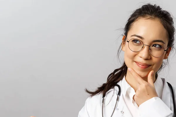 Gesundheitswesen, Medizin und Apothekenkonzept. Porträt einer nachdenklichen, zufriedenen asiatischen Ärztin, die lächelt und aufblickt, zufrieden denkt, Tabletten in der Hand hält, neue Medikamente erfindet, um kranke Menschen zu heilen — Stockfoto