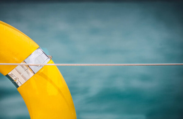 Close-up Yellow life ring hanging on boat with ocean background.