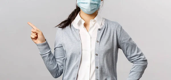 Covid19, concepto de virus, salud y medicina. Retrato de una joven asiática de aspecto serio con máscara médica, prevenir la propagación del coronavirus y la gripe, apuntando a la izquierda, mostrando información sobre la enfermedad — Foto de Stock