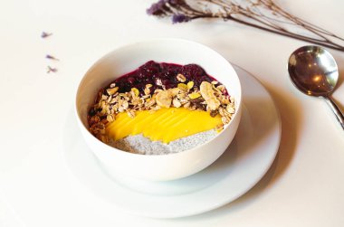 Kahvaltının üzerine yabanmersini, badem, muz ve chia tohumları konmuş meyve suyu kasesi..