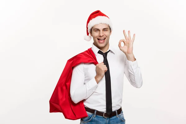 クリスマスのコンセプト-ハンサムなビジネスマンは陽気なクリスマスを祝い、幸せな新年はサンタの赤い大きな袋でサンタの帽子を着用. — ストック写真
