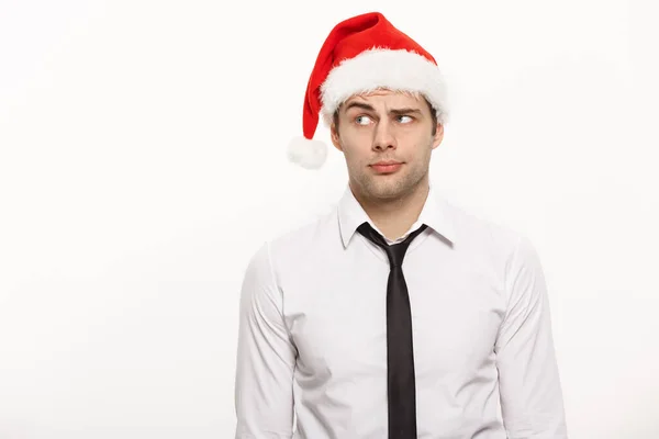 Noel kavramı - Yakışıklı bir iş adamı beyaz izole edilmiş arka planda düşünceli bir yüz ifadesiyle Noel Baba şapkası takar. — Stok fotoğraf