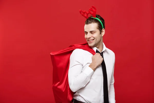 Рождество - красивый деловой человек празднует веселый праздник и счастливый Новый год в оленьей прическе, держа в руках красную большую сумку Санты . — стоковое фото