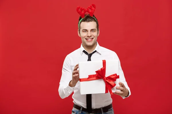 Weihnachtskonzept - Fröhlich fröhlicher junger Geschäftsmann mit dekorativem Geschenk auf rotem Hintergrund. — Stockfoto