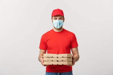 Çevrimiçi dağıtım ve Coronavirus Kavramı. Beyaz stüdyo arka planında izole edilmiş halde pizza kutuları tutan maskeli neşeli genç teslimatçı.
