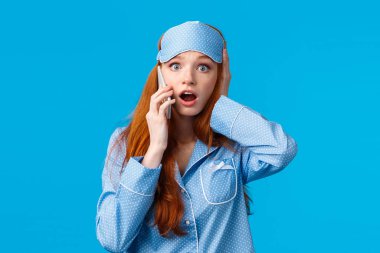 Haberler kötü. Şok olmuş ve endişeli genç bir kız kötü bir şey duyuyor, telefonla konuşuyor, kafası karışmış, nefes nefese kalmış, soluk soluğa kalmış ve kameraya bakıyor şaşkın, mavi arka plan