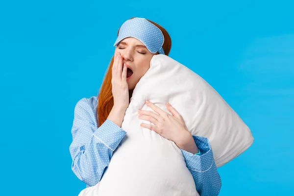 Feminine and glamour lovely redhead teenager yawning and cover opened mouth, feeling sleepy and tired got to bed, hugging pillow, close eyes having good night, standing blue background — Stock Photo, Image