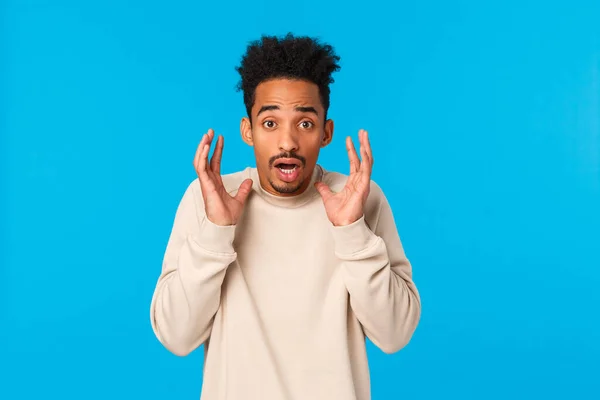Man in panic telling something terrible, bad news. Alarmed, scared, shocked african-american guy witness accident, raising hands near face frightened and startled, gasping concerned, blue background — Stock Photo, Image