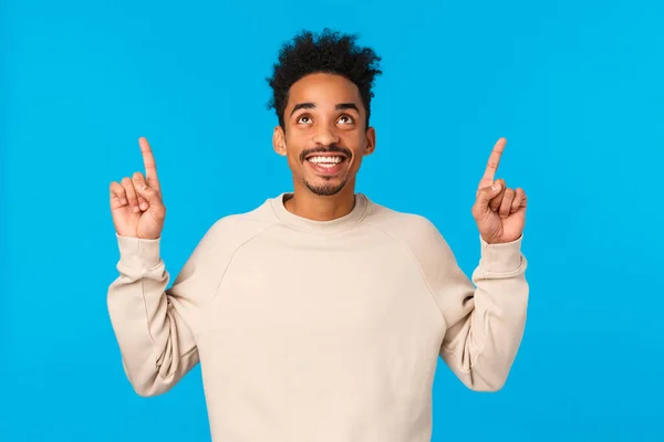 Wonderful promo. Amazed, excited smiling happy african american man with afro hipster haircut, moustache, looking pointing up admiring view, found excellent gift for valentines day, blue background — Stock Photo, Image