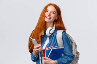 Neşeli, arkadaş canlısı ve karizmatik kızıl saçlı kadın neşe içinde gülüyor, arkadaşlarına mesaj atıyor, akıllı telefonlarla sohbet ediyor, üniversite hayatının tadını çıkarıyor, sırt çantası ve not defterleriyle kampüse gidiyor.