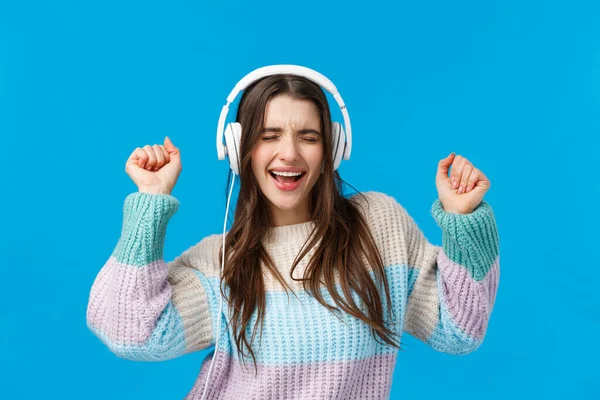 Rock and roll baby. Mujer morena carismática emotiva despreocupada disfrutando escuchando música en nuevos auriculares de regalo, bailando levantando las manos, cerrando los ojos y cantando junto a la canción favorita, fondo azul — Foto de Stock