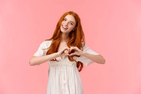 Waist-up portrait lovely, romantic and cute european woman with red hair, tilt head and smiling, saying love you, make heart gesture in like, express affection or sympathy, happy valentines day — 스톡 사진