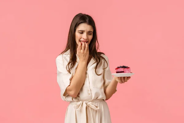 Não resisto à tentação. Jovem mulher em dieta, tentando comer comida saudável quer morder delicioso bolo de mirtilo, mordendo as unhas e olhando para o prato, de pé fundo rosa com desejo — Fotografia de Stock