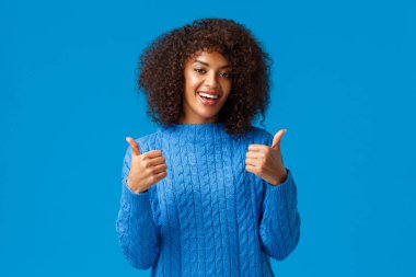Everything super cool. Cheerful and satisfied african american woman with afro haircut, smiling and showing thumbs-up in approval, like product, recommend software or app, standing blue background clipart
