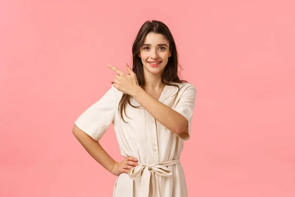 Optimistisch prachtig brunette Kaukasische vrouwelijke shoppaholic, wijzen linksboven hoek en lachend assertief met enthuiastic positieve grijns, staande roze achtergrond vrolijke — Stockfoto