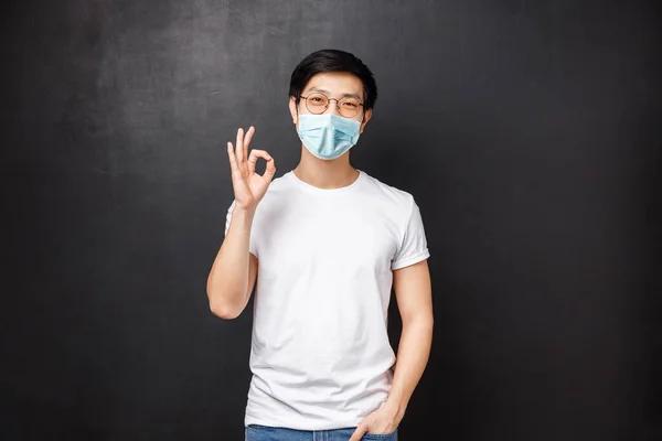 Retrato de guapo sonriente joven moderno asiático estudiante masculino en gafas de sol y camiseta, confirmar o garantizar la calidad perfecta, mostrar signo bien, de acuerdo con la persona, como producto —  Fotos de Stock