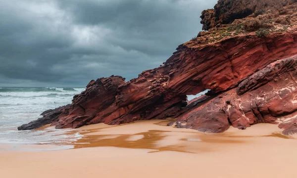 Red ocean rocks at the beach in cloudy weather light. Praia da Bordeira. Carrapareira, Algarve Coast in Portugal, Atlantic Ocean