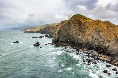 San Francisco kıyı şeridi. Sausalito, California, ABD 'deki Marin Burunları' ndaki kayalıklardan görülen Point Bonita Deniz Feneri yakınlarındaki okyanus ve sahil kayalıkları..