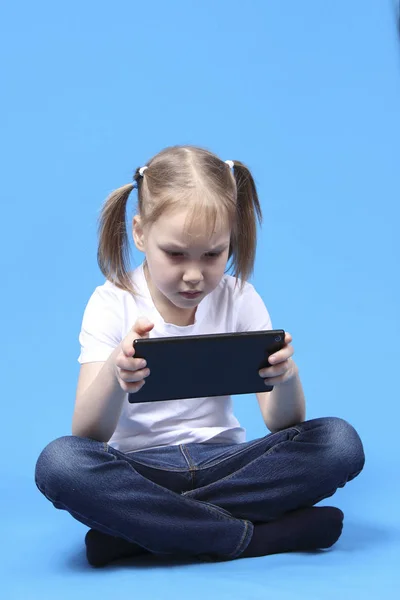 Dziewczyna siedzi i gra na tablecie. na białym tle na niebieskim tle — Zdjęcie stockowe