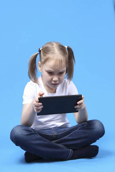 Kız oturur ve tablet üzerinde çalış. üzerinde mavi arka plan izole
