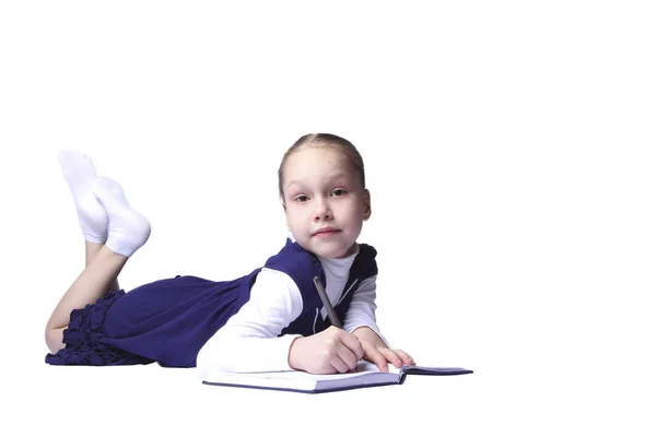 Liten flicka ligger och skriver i en anteckningsbok på vit bakgrund — Stockfoto