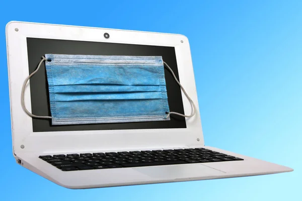 屏幕上有蓝色医疗面具的笔记本电脑 背景为浅蓝色 Coronavirus Covid 19流行病 — 图库照片