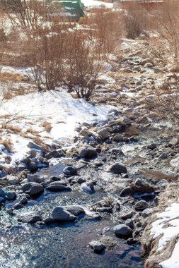Taşlar, kar ve çıplak ağaçlar arasında soğuk bir nehir akar