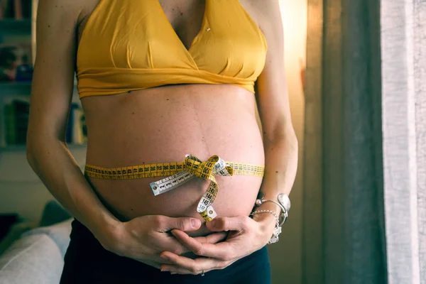 Pancia di giovane donna incinta con fiocco regalo con metro a nastro. P — Foto Stock