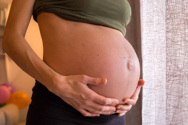 Pregnant woman holds her hands on her swollen belly. Motherhood