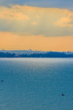 Bulutların arasından güneş ışınları kırmak bulutlu gün sabahı güzel gündoğumu denize. Sen zum yapıldığında aracılığıyla bulutlar ile kentsel peyzaj, ışık saçan güneş küçük balıkçı tekneleri göreceksiniz.
