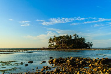 Rock plaj ve deniz suyu mavi gökyüzü ve bulutlu gün arka plan gerilemiştir zaman ağaç ile yalnız uzak ada