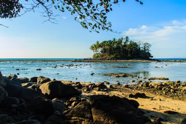 Rock plaj ve deniz suyu mavi gökyüzü ve bulutlu gün arka plan gerilemiştir zaman ağaç ile yalnız uzak ada