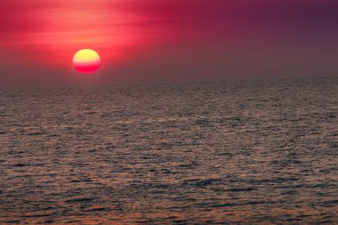Güzel gün batımı deniz, sahilden görüntülemek. Alacakaranlıkta sakin deniz bulanık dramatik gökyüzü arka plan üzerinde yuvarlak ve parlak güneşte.