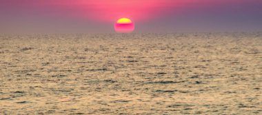 Güzel gün batımı deniz, sahilden görüntülemek. Alacakaranlıkta sakin deniz bulanık dramatik gökyüzü arka plan üzerinde yuvarlak ve parlak güneşte.