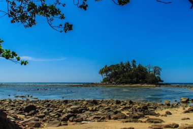 Rock plaj ve deniz suyu mavi gökyüzü ve bulutlu gün arka plan gerilemiştir zaman ağaç ile yalnız uzak ada