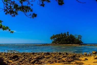 Rock plaj ve deniz suyu mavi gökyüzü ve bulutlu gün arka plan gerilemiştir zaman ağaç ile yalnız uzak ada